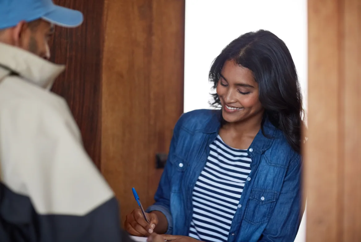 A smiling customer signing for a prescription delivery at her front door