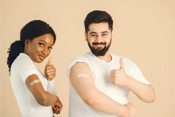 Two smiling adults giving a thumbs-up, showing bandages on their arms after getting vaccinated